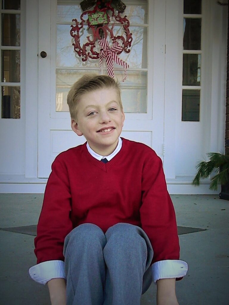 Boy on a front porch in red sweater
